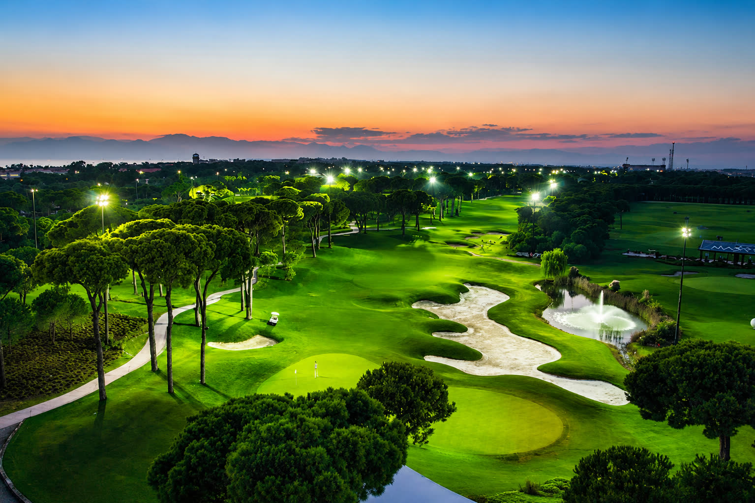 Floodlit golf green under an orange evening sky
